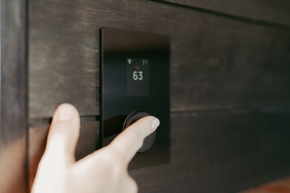A hand adjusting a wall thermostat set to 63 degrees